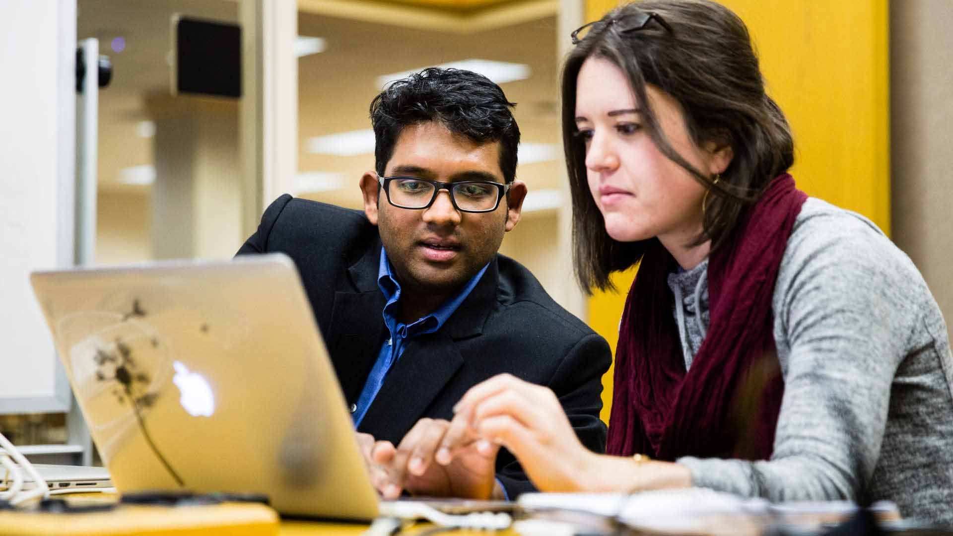 Two students look at a laptop together.