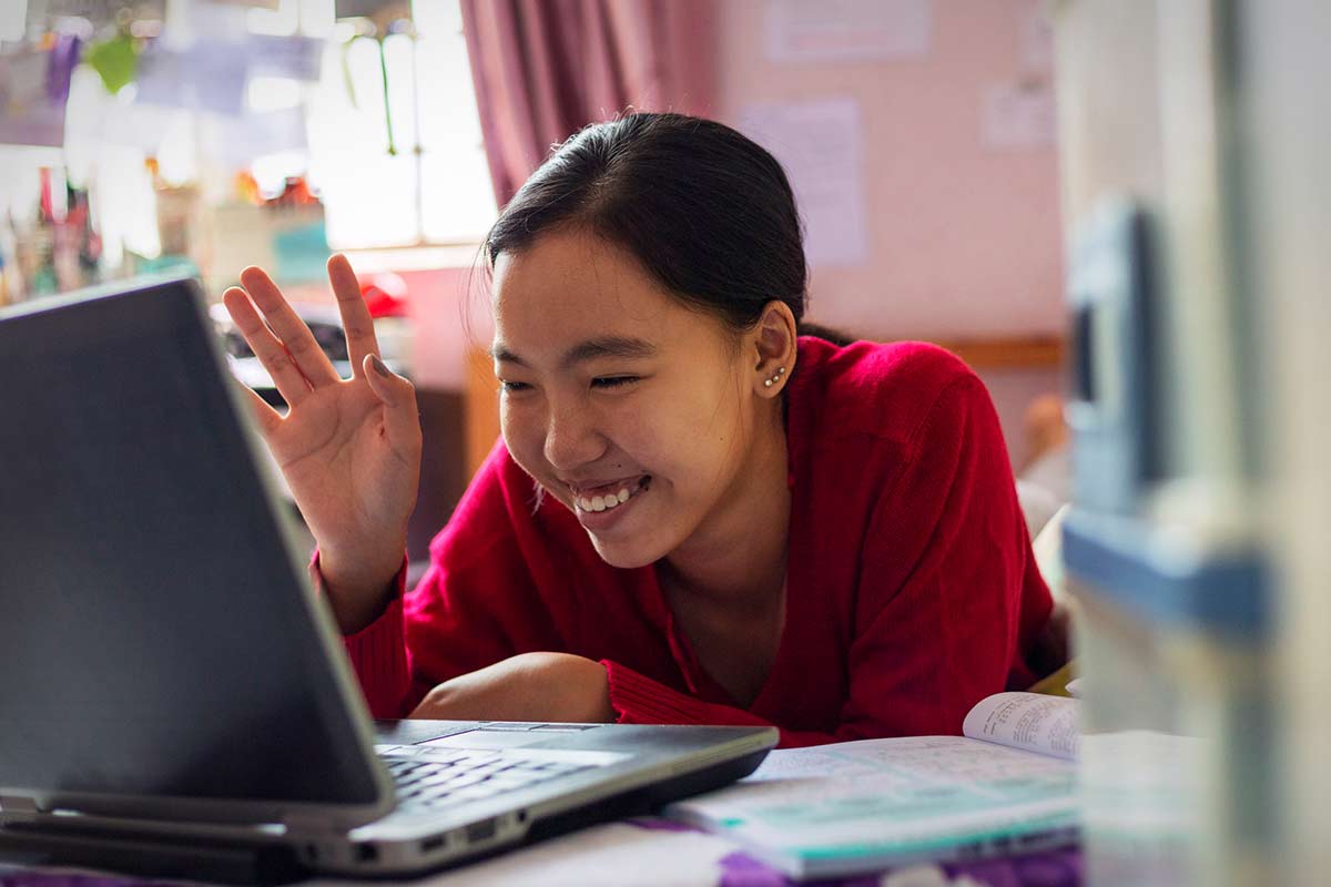 Female smiles and waves at her computer.