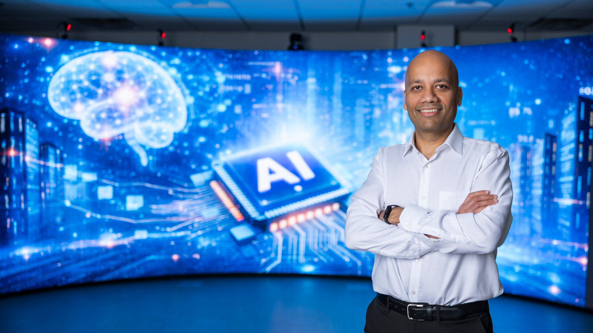 Pictured: Dr. Manjeet Rege, Professor and Chair of the Software Engineering and Data Science department at the University of St. Thomas stands in front of a 3D screen showing a digital AI display.