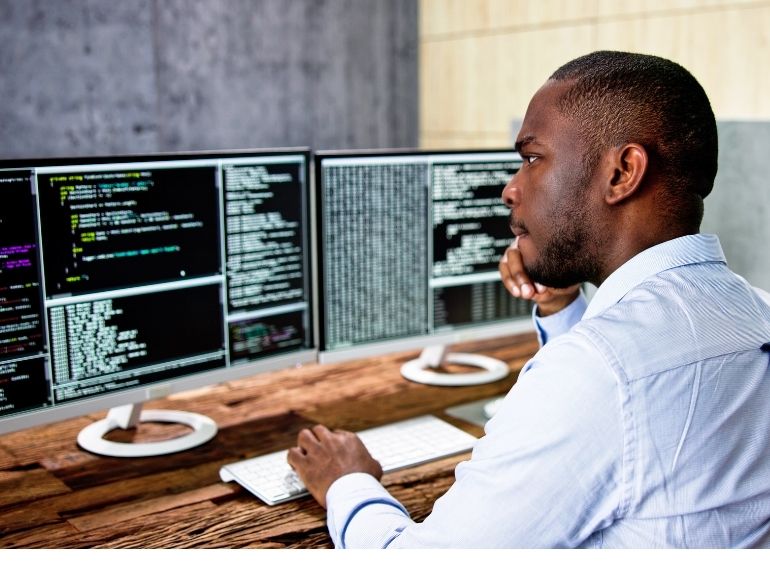 Individual sits in front of computers.