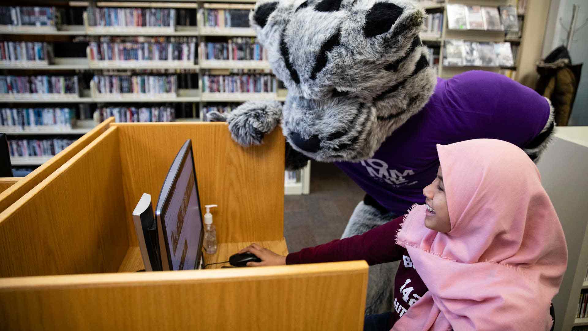 Tommie mascot and student looking at a computer.