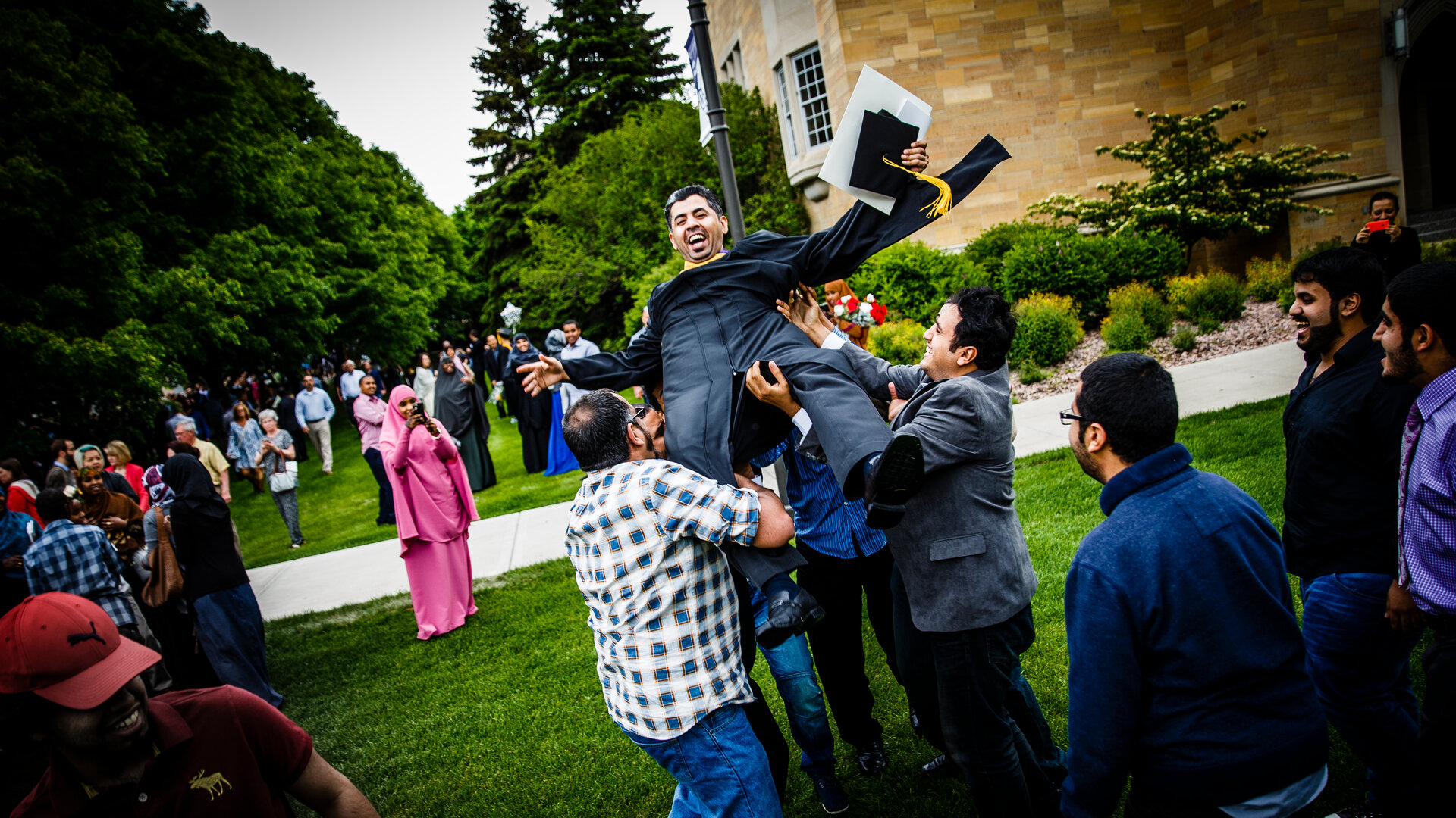 Family and friends of international student playfully toss them in the air after graduation.